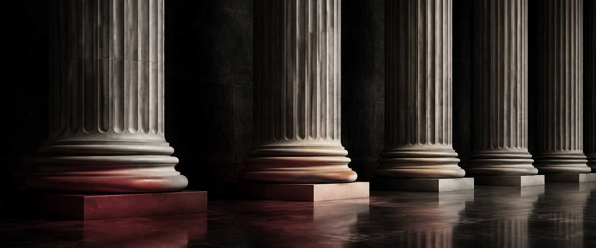 Classical stone columns with restrained maroon accents in a dark architectural setting
